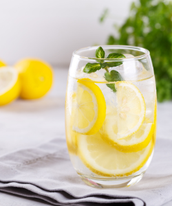 Sklenený pohár s citrónovou vodou a čerstvou mätou. Citrónová voda pomáha pri detoxikácii a udržiavaní zásaditého prostredia v tele, čo je dôležité pre prevenciu premnoženia kvasinky Candida.