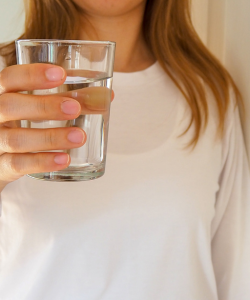 Pohár čistej vody držiaci v ruke ako symbol správnej hydratácie. Dostatok vody je kľúčový pre prevenciu dehydratácie a reguláciu krvného tlaku vďaka správnej funkcii obličiek.