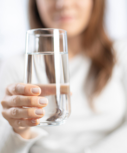 Žena držiaca pohár čistej vody ako symbol správnej hydratácie tela. Voda je základom pre zdravie a prevenciu ochorení.